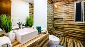 A modern bathroom with a large white bathtub, a toilet, and a shower area with a wooden wall design. - The Furlough Fur304 (Playa del Carmen)