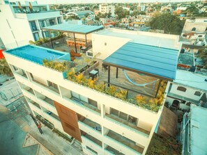 A multi-story building with a rooftop pool, outdoor seating area, and a covered terrace.