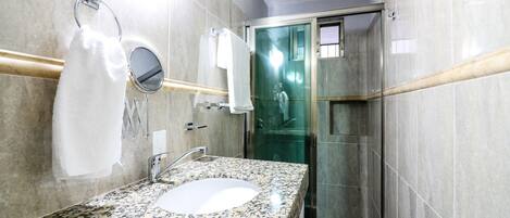 A bathroom with a granite countertop sink, a mirror, a towel rack, and a glass shower enclosure.