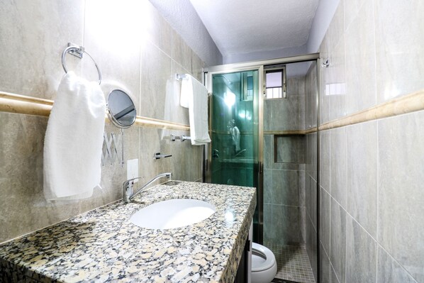 Une salle de bain dotée d’un lavabo avec un plan de travail en granit, d’un miroir, d’un porte-serviettes et d’une cabine de douche en verre.
