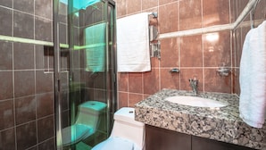 A bathroom with a glass shower enclosure, a white toilet, a granite countertop sink, and a towel rack. - Studio Fogon Fog009 (Playa del Carmen)