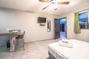 A bedroom with a bed, a desk, and a chair. There is a ceiling fan, a TV, and a window with curtains.
