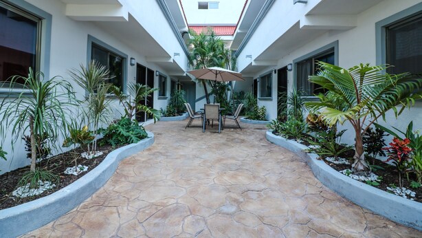 A courtyard with a stone floor, surrounded by planters with various plants, a central table with chairs, and an umbrella. - Studio Fogon Fog009 (Playa del Carmen)