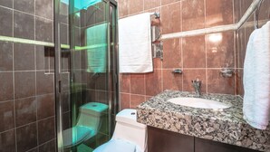 A bathroom with a glass shower enclosure, a white toilet, a granite countertop sink, and a towel rack. - Studio Fogon Fog013 (Playa del Carmen)