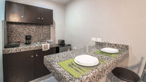 A compact kitchen with granite countertops, a coffee maker, a toaster, and a sink. There are two plates and cutlery on a green placemat. - Studio Fogon Fog013 (Playa del Carmen)