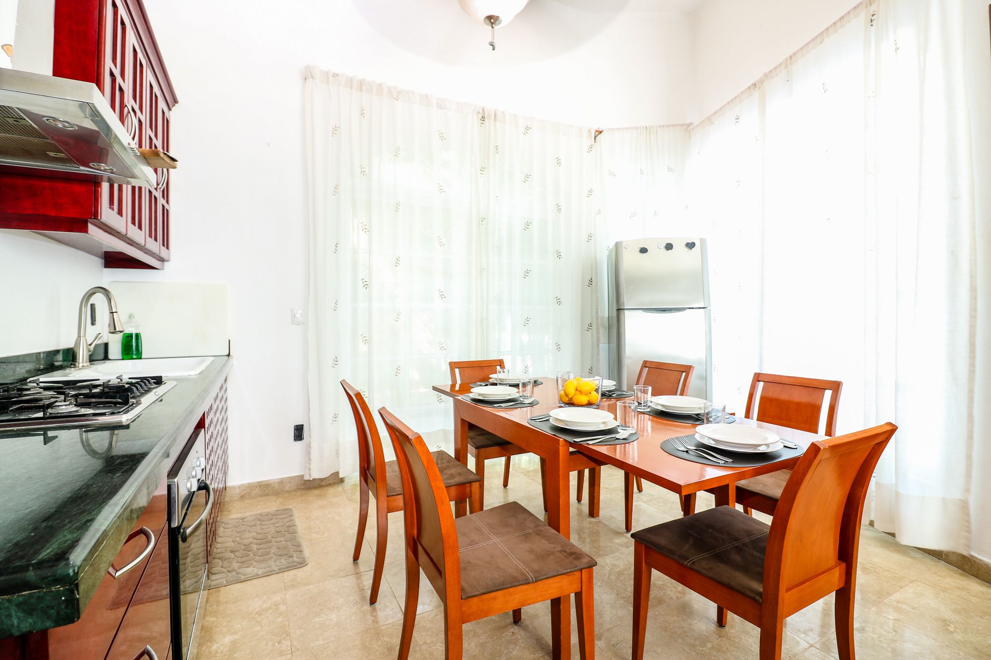 A compact kitchen with a stove, sink, and refrigerator. A dining table with chairs is set up in the room.