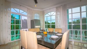 A dining area with a large table set for six, surrounded by six chairs, with a refrigerator and a vase of lemons on the table. - Apartment Castello 1C (Playa del Carmen)