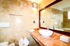 Ein Badezimmer mit beigen Fliesen, einem großen Spiegel, einem Waschbecken, einem Bidet und einem Handtuchhalter.