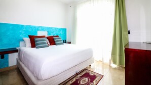 A bedroom with a bed, a nightstand, a ceiling fan, a window with curtains, and a red piece of furniture. - Apartment Castello 1C (Playa del Carmen)