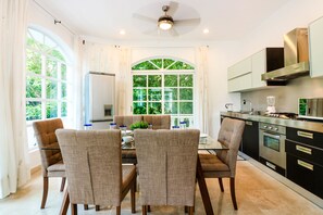 A modern kitchen with a dining area, large windows, and a ceiling fan.