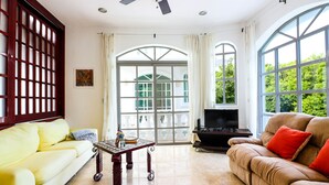 Un salón amplio con un sofá amarillo, un sofá marrón con cojines rojos, una mesa de centro y un televisor sobre un mueble.