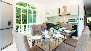 Una cocina moderna con una mesa de comedor de cristal, sillas tapizadas en gris y vistas a la vegetación a través de un amplio ventanal.