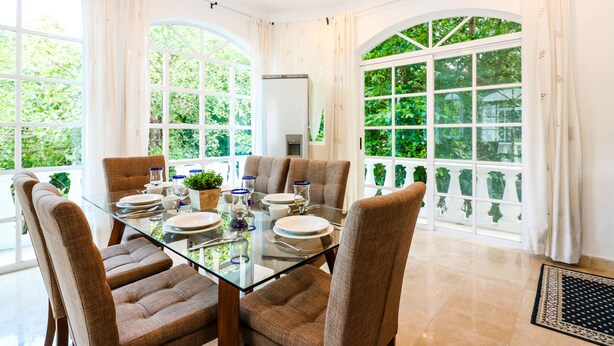 Un comedor con una mesa de vidrio, sillas tapizadas en tono café y vista a la vegetación a través de amplias ventanas.