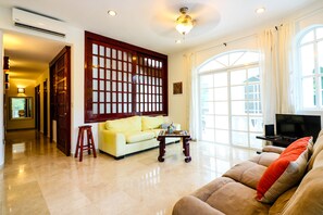 A spacious living room with a yellow sofa, a brown sofa with a red pillow, a wooden coffee table, and a TV on a stand.