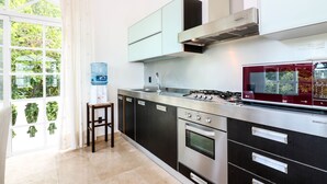 A modern kitchen with stainless steel appliances, a water dispenser, and a view of greenery through the window. - Apartment Castello 2C (Playa del Carmen)