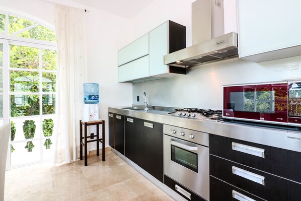 A modern kitchen with stainless steel appliances, a water dispenser, and a view of greenery through the window.