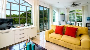 A spacious living room with a yellow sofa, large windows, and a flat-screen TV on a white cabinet. - Apartment Castello 2C (Playa del Carmen)