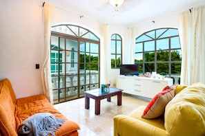 A spacious living room with large windows, a flat-screen TV, and comfortable seating.