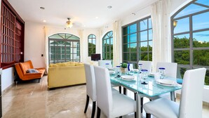 A dining area with a glass table, white chairs, and a yellow sofa. - Apartment Castello 2C (Playa del Carmen)