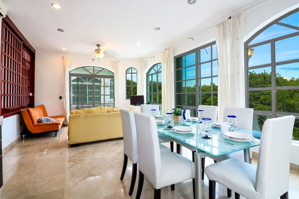 A dining area with a glass table, white chairs, and a yellow sofa.