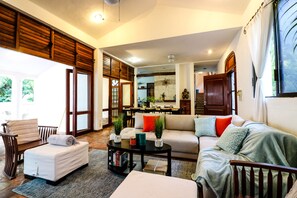 A spacious living room with a sofa, a coffee table, and a reading chair. There is a dining area visible in the background. - Villa 4 Soles (Playa del Carmen)