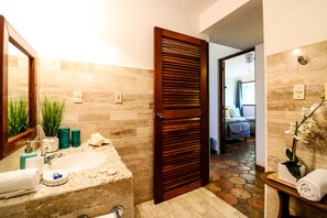 A bathroom with a stone sink, a mirror, and a wooden door. - Villa 4 Soles (Playa del Carmen)