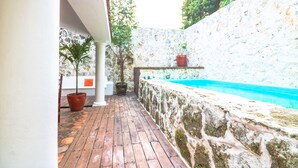 A wooden deck with a stone wall and a pool. - Villa 4 Soles (Playa del Carmen)