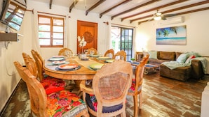 Un coin repas avec une table en bois dressée pour six personnes, entourée de fauteuils richement décorés et recouverts d’un tissu à motifs floraux.