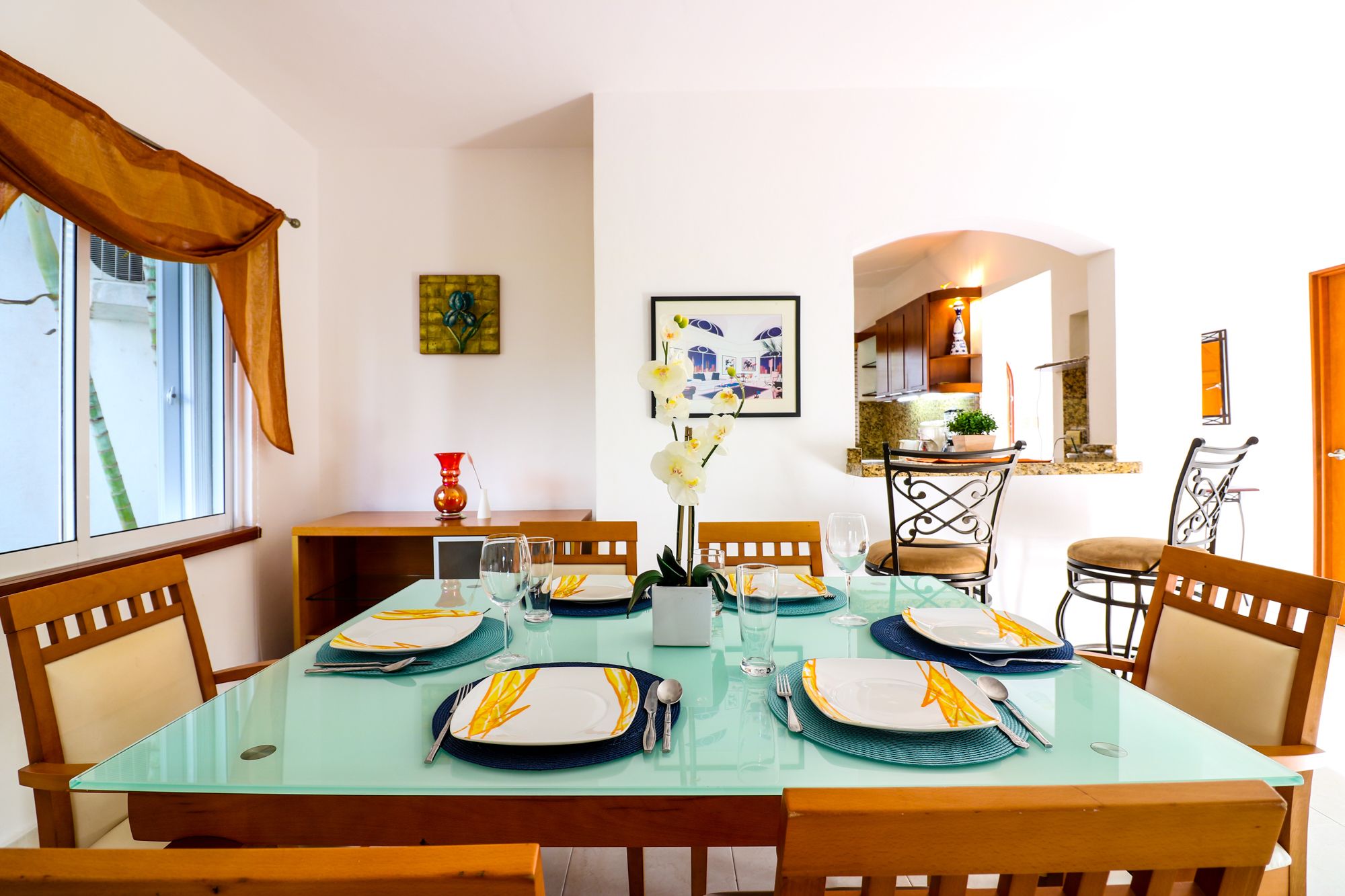 A dining area with a glass table set for four, surrounded by wooden chairs.