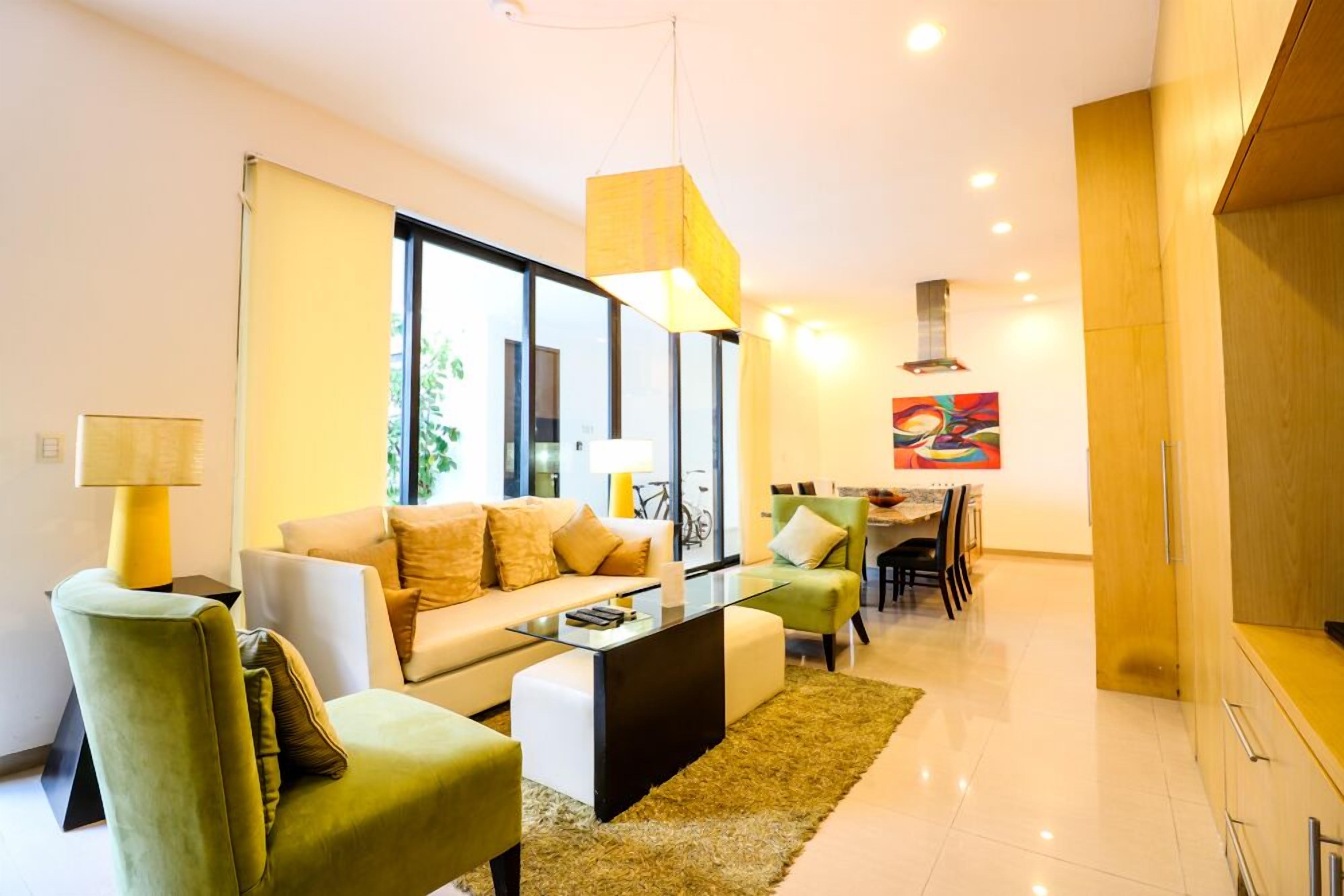 A modern living room with a sofa, chairs, a glass coffee table, and a dining area with a table and chairs.