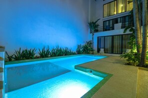 A swimming pool with a tiled edge, surrounded by plants and a building with large windows and a balcony. - Apartment Habita Combo (Playa del Carmen)