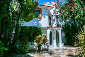 A white building with a tiled roof, surrounded by lush greenery and flowering plants. - Casa 20 (Playa del Carmen)