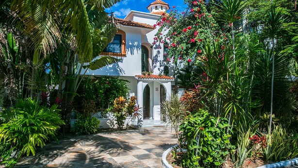 A white building with a tiled roof and arched windows, surrounded by lush tropical plants and a checkered stone pathway. - Casa 20 (Playa del Carmen)