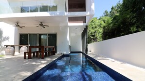 Uma área de piscina moderna ao ar livre, com um banco de madeira e duas ventoinhas no teto.