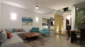 Sala de estar moderna com sofá cinzento, poltronas verde-água e mesa de centro de madeira. Um quadro com uma cena de praia está pendurado na parede.
