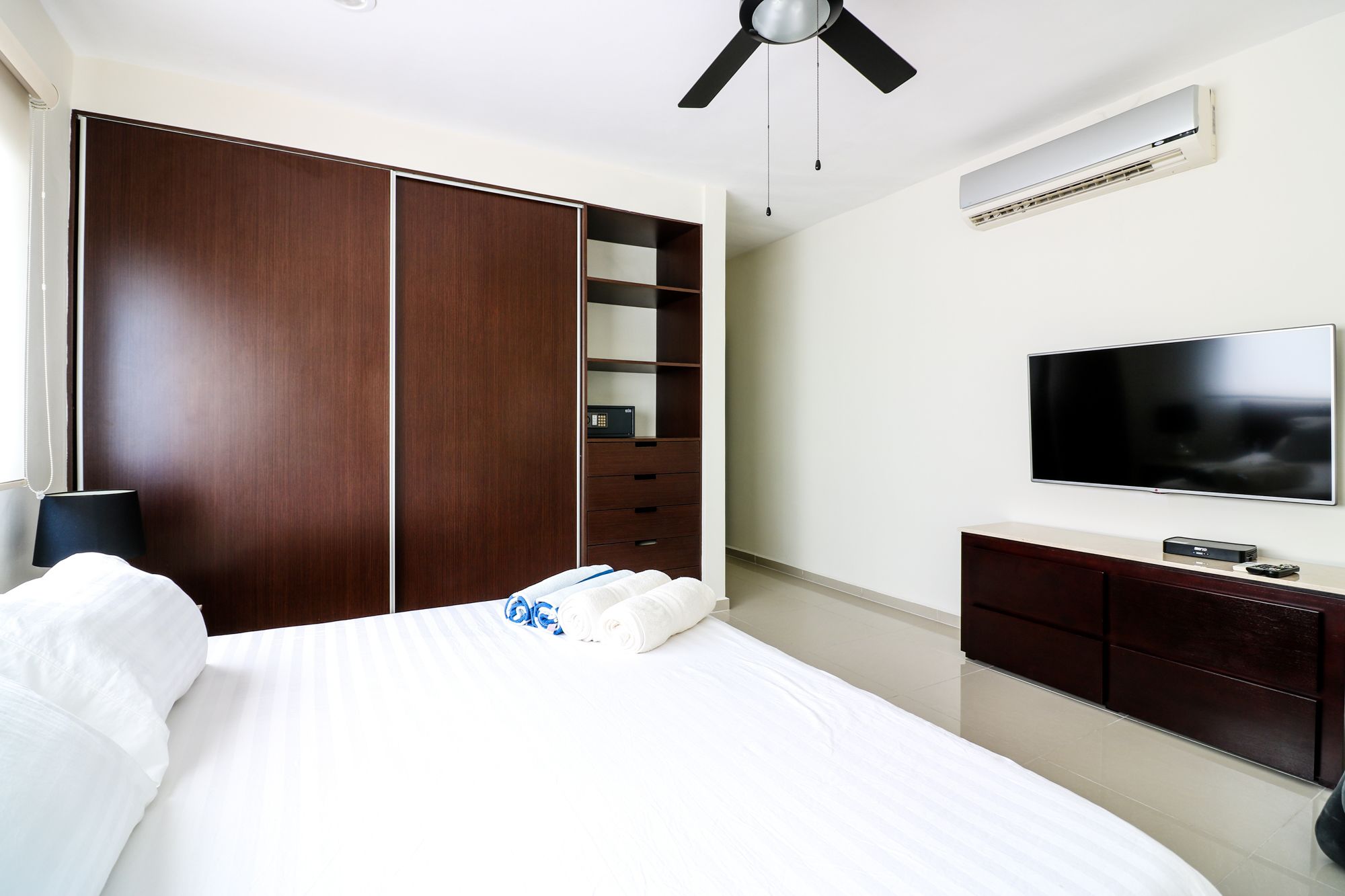 A hotel room with a bed, a wardrobe, a television, and an air conditioning unit.