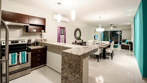 A modern kitchen with granite countertops, a built-in oven, and a dining area with a white table and chairs. - Apartment Sabbia B402 (Playa del Carmen)