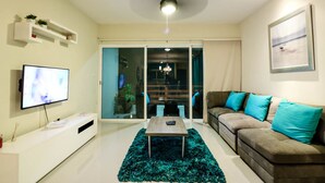 A modern living room with a flat-screen TV, a sofa with teal cushions, a coffee table, and a sliding glass door leading to a balcony. - Apartment Sabbia B402 (Playa del Carmen)