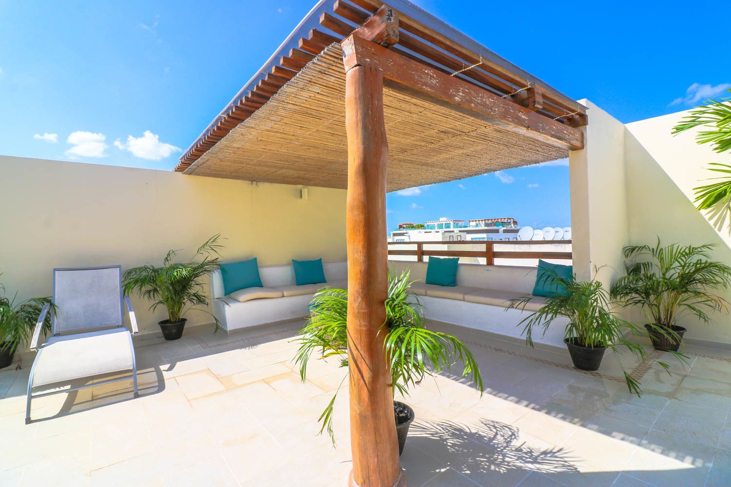 Eine Dachterrasse mit einer Holz-Pergola, einem weißen Sofa mit türkisfarbenen Kissen und Topfpflanzen.