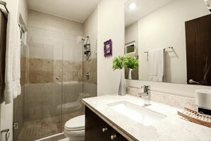 Een moderne badkamer met een douchecabine van glas, een wit toilet en een wastafel met een grote spiegel.