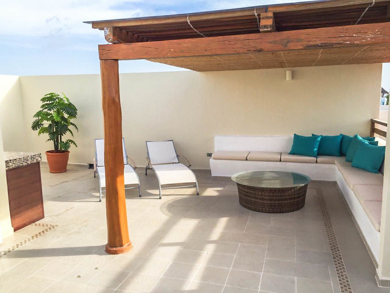 Un patio al aire libre con un sofá blanco, dos sillas blancas, una mesa de centro de mimbre y una planta en maceta.