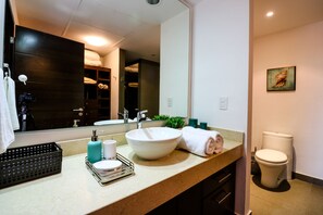 Un baño moderno con un espejo grande, un lavamanos y un inodoro. Hay un perchero y una pequeña planta en la encimera.