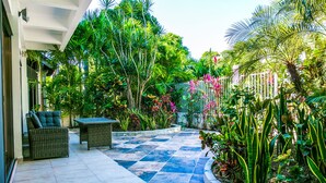 A patio with a checkered tile floor, wicker furniture, and lush tropical plants. - Villa Compound (Playa del Carmen)