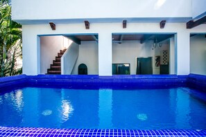 Una piscina con baldosas azules, una escalera que sube a un nivel superior y una puerta a una habitación.