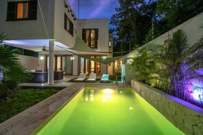 A modern pool area with a green pool, lounge chairs, and a covered seating area.