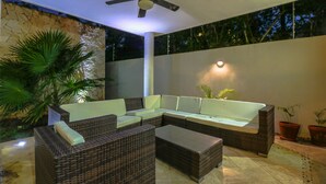 Un espace extérieur moderne, aménagé avec des meubles en osier, un ventilateur de plafond et un mur en pierre.