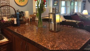 A kitchen with a copper coin mosaic backsplash, a vase with red flowers, and a decorative plate with a moose design on the wall.