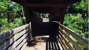 A wooden covered bridge with a sloped roof, surrounded by lush greenery.