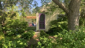 A house with a garden path leading to a purple door, surrounded by lush greenery.
