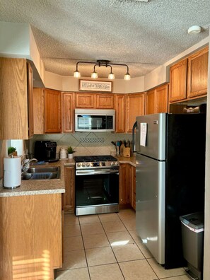 A kitchen with wooden cabinets, a stainless steel refrigerator, a microwave, an oven, and a sink.